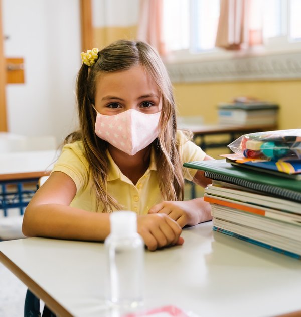 girl_sitting_at_her_chair_and_table_in_the_classroom_wearing_a_mask_to_protect_herself_during_the...
