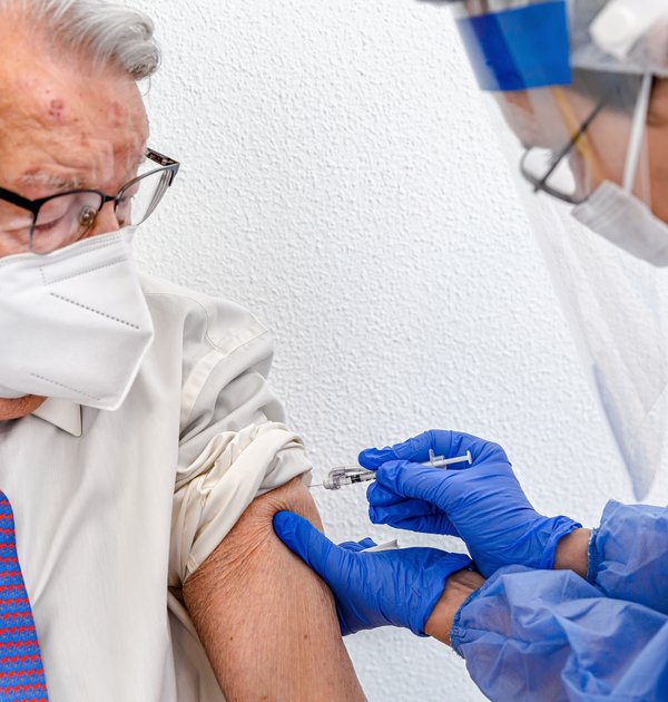 elderly_man_in_mask_watches_as_nurse_in_protective_suit_and_covid_mask_gives_him_coronavirus_vaccine